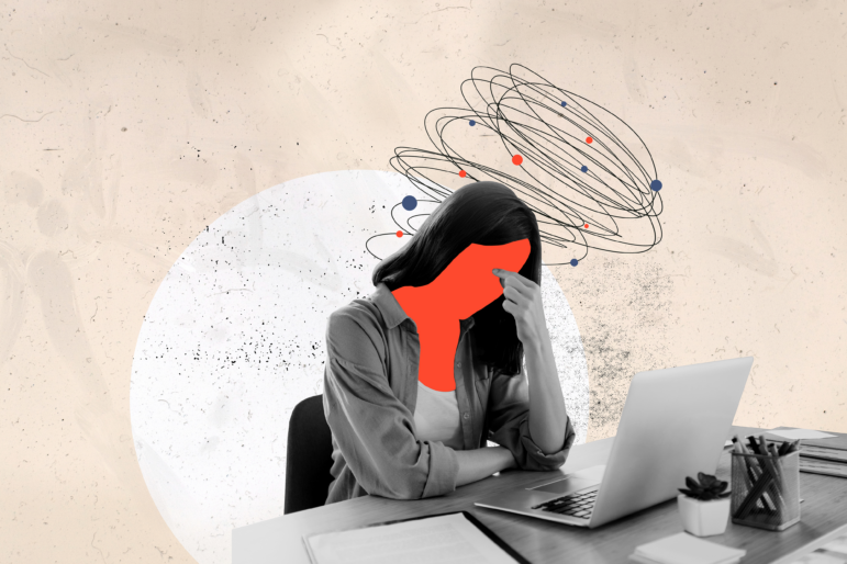 In this photo illustration, a woman sits at a desk in front of a laptop computer. She's leaning forward, with her left elbow on the desk and her left hand supporting her forehead.