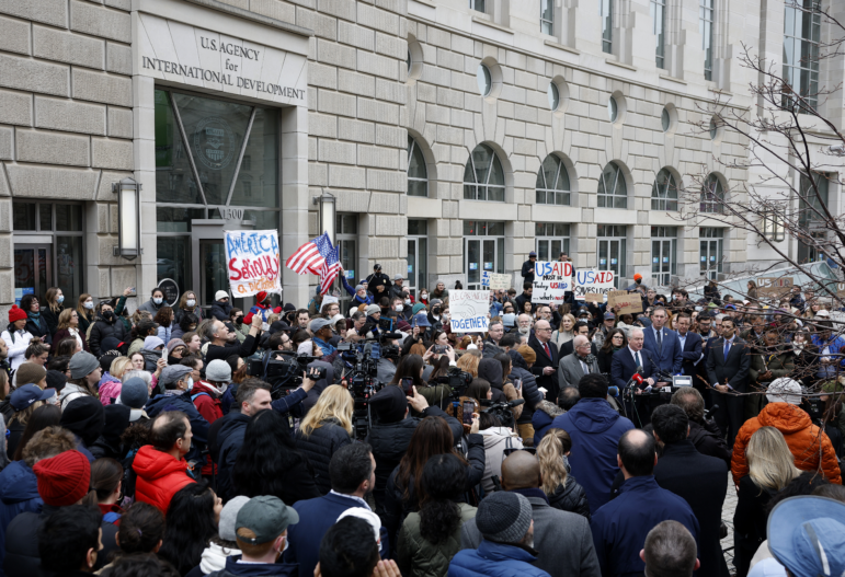 In this photo, supporters of the U.S. Agency for International Development demonstrate outside USAID's headquarters building in Washington, D.C. The people are gathered in a crowd, and some are holding signs.
