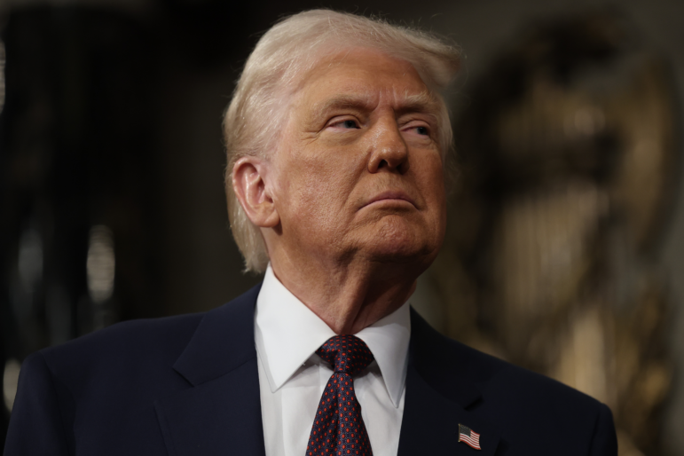 This photo shows President Trump photographed from about the shoulders up. He's wearing a dark blue suit with an American flag pin.