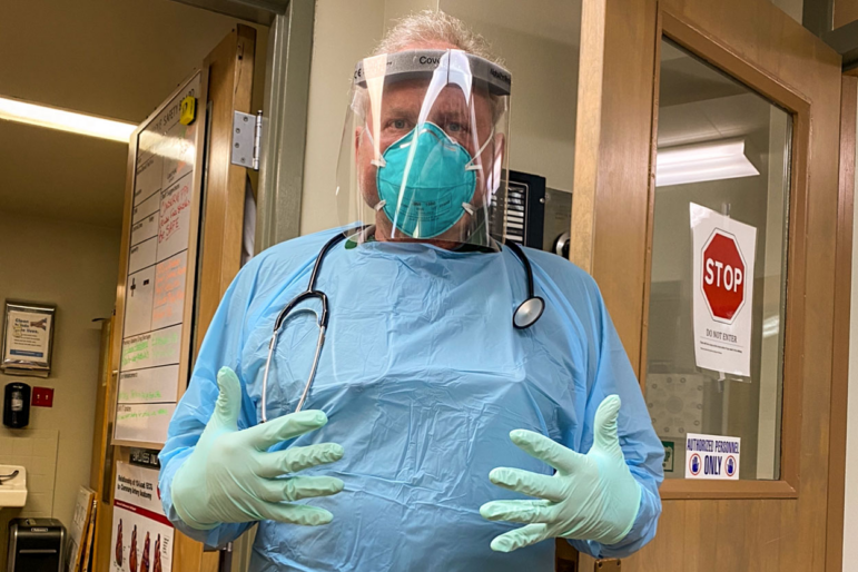 Dr. Kurt Papenfus in 2020 is shown wearing surgical scrubs, gloves, a mask and a plastic shield over his face.
