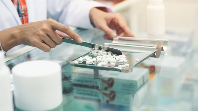 Medicine tablets on counting tray with counting spatula at pharmacy.