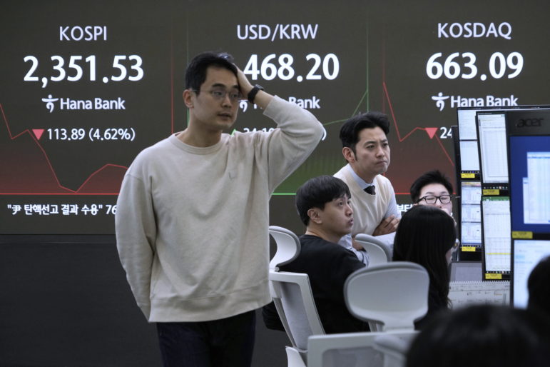 Currency traders work near a screen showing the Korea Composite Stock Price Index (KOSPI), top left, and the foreign exchange rate between U.S. dollar and South Korean won, top center, at the foreign exchange dealing room of the KEB Hana Bank headquarters in Seoul, South Korea, Monday, April 7, 2025.