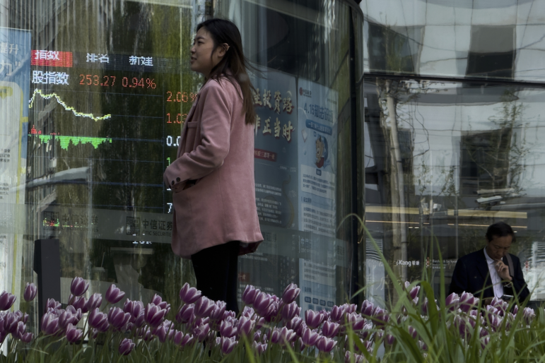 People stand outside a brokerage house as an electronic board displays shares trading index in the Central Business District, in Beijing on Thursday.