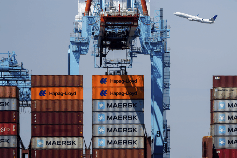 An airplane flies over the container ship Alexandra at the Port Newark Container Terminal on April 18 in Newark, N.J.