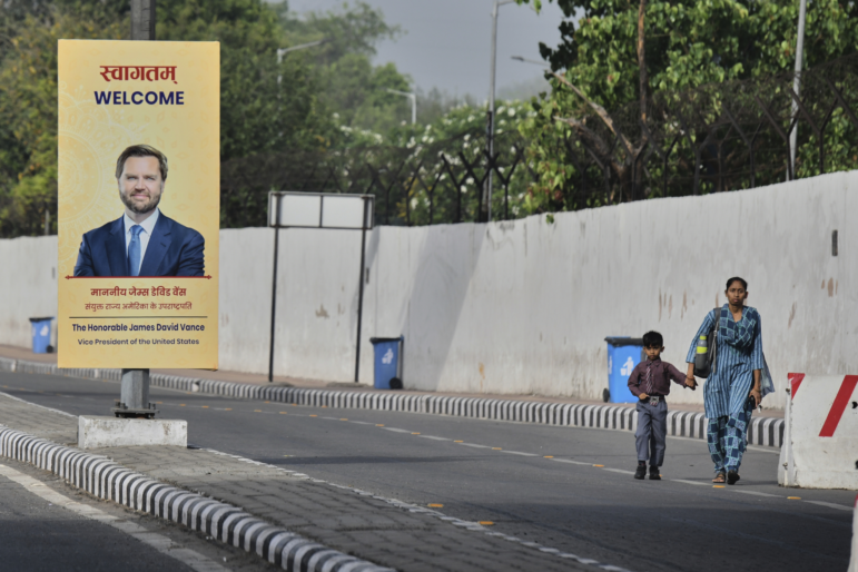 A woman and a child walk past a banner welcoming U.S. Vice President JD Vance on a street in New Delhi, India, on Monday.
