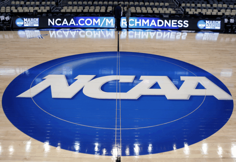 The NCAA logo is displayed in 2015 at the center of the basketball court at The Consol Energy Center in Pittsburgh, with a March Madness ad displayed on sideline screens behind it.
