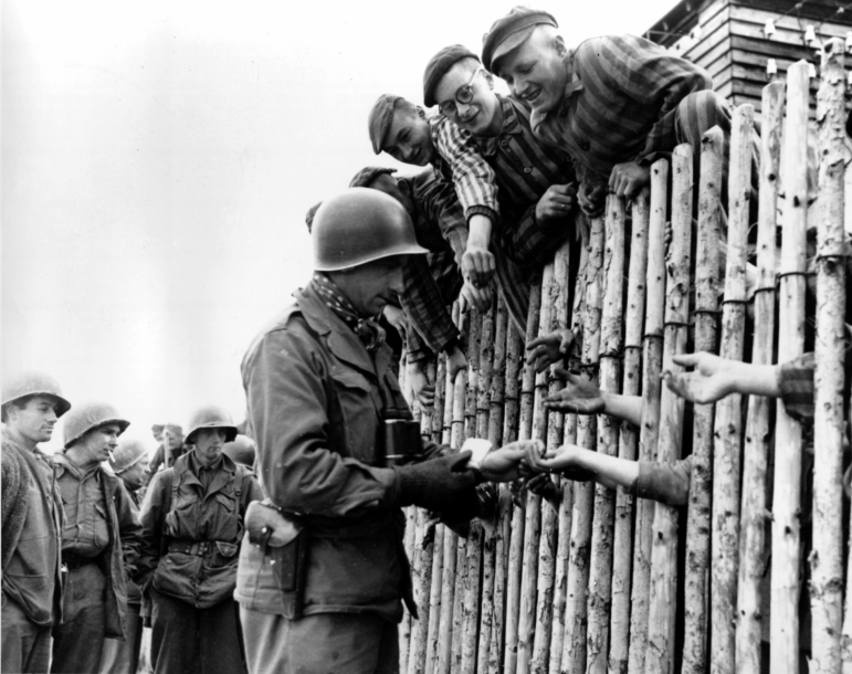 A still from a documentary film shows a U.S. soldier reaching out to outstretched hands of prisoners of the liberated Nazi concentration camp at Dachau, in then West Germany, in April 1945, during World War II.