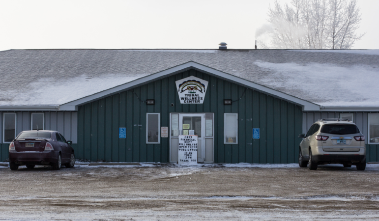 A modest building with some snow on the roof and two cars parked in front of it is shown.