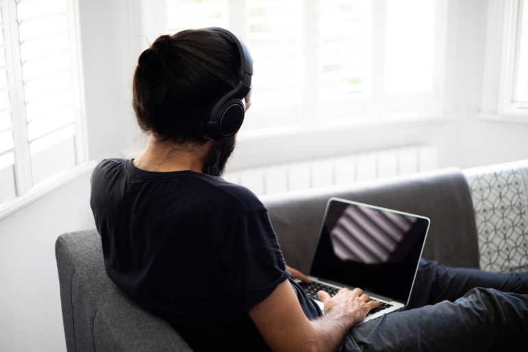 A man with his back to the camera uses a laptop and wears headphones.