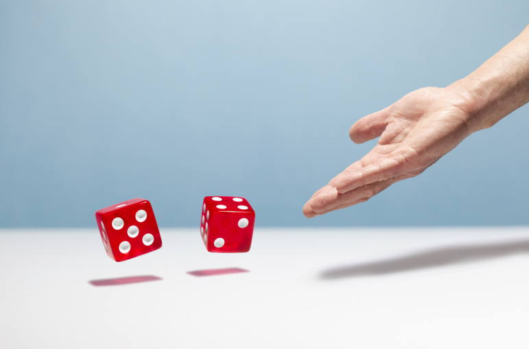 A man's hand is shown throwing a pair of red dice.