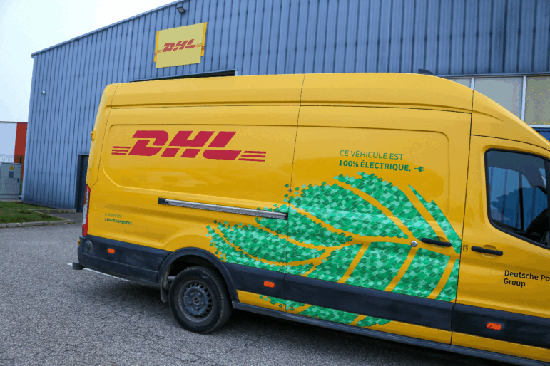 A yellow and red DHL delivery vehicle with a green leaf pattern on it is seen in front of a warehouse in Valence, France, in December 2024.