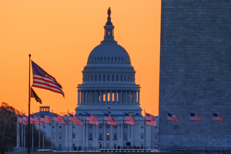 Sunrise turns the sky orange behind the U.S. Capitol building as it illuminates the U.S. Flags circling the base of the Washington Monument  in Washington, D.C.