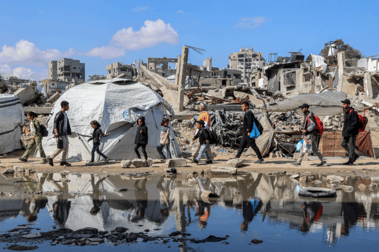 People walk by a tent shelter near the rubble of a collapsed building in western Gaza City on April 15.