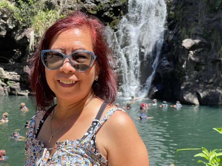 This is a photo of Lewelyn Dixon. She's wearing sunglasses and a sleeveless outfit, and she's standing in front of a waterfall.