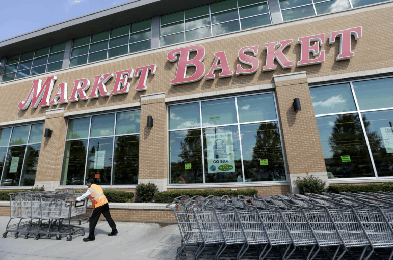 A worker in an orange vest gathers shopping carts in front of a Market Basket store.