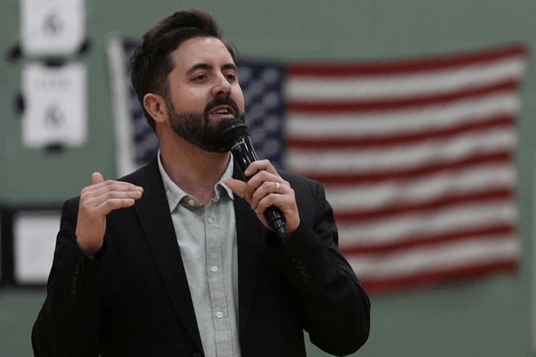 Cory Bowman preaches in a gymnasium against an American flag.