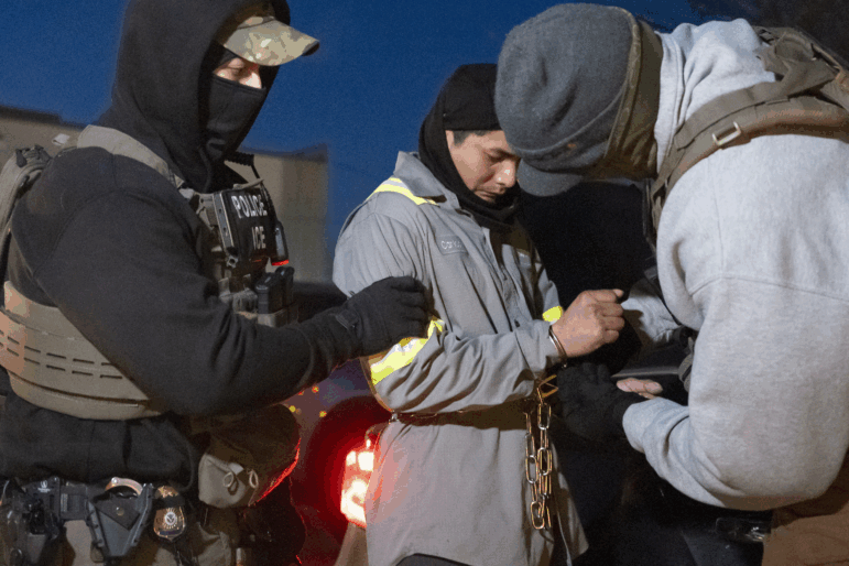U.S. Immigration and Customs Enforcement officers use a chain to more comfortably restrain a detained person using handcuffs positioned in front.