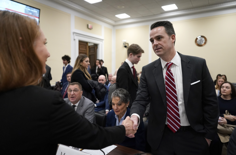 Stewart Whitson, wearing a suit and tie, shakes the hand of a lawmaker in a congressional hearing room.
