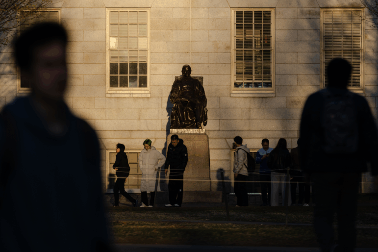 People gather to take photos with the John Harvard statue at Harvard University. President Trump made another threat to Harvard's tax-exempt status in a social media post on Friday.