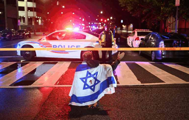 A man draped in the Israeli flag, bearing a cross and the name "Jesus" at its center, gestures as Metropolitan Police officers secure the area outside the Capital Jewish Museum in Washington, D.C. Two Israeli embassy staffers were shot dead late Wednesday by an alleged gunman who shouted "free Palestine."