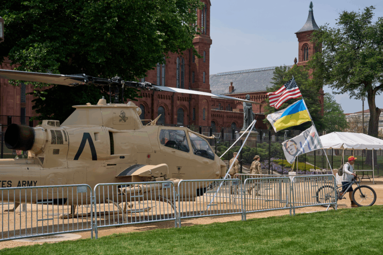 A man bicycles with several flags past a helicopter on display during preparations for an upcoming military parade commemorating the Army's 250th anniversary and coinciding with President Donald Trump's 79th birthday.