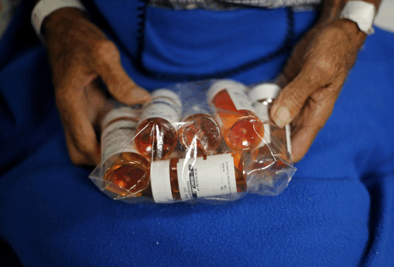 A person holds a plastic bag filled with prescription pill bottles.