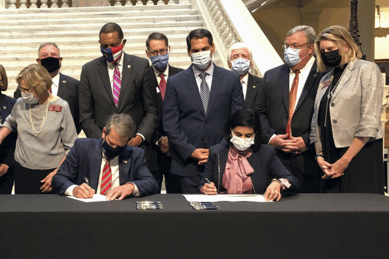 Georgia Gov. Brian Kemp, left, and Centers for Medicare and Medicaid Services Administrator Seema Verma, right, sign waivers allowing Georgia to institute work requirements for certain Medicaid recipients at the state Capitol in Atlanta, Oct. 15, 2020.