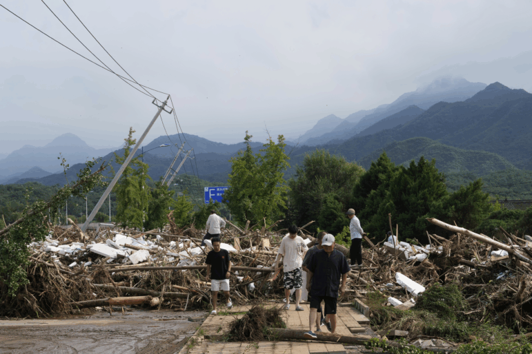 Local residents walks in front of a damaged road littered with broken tree branches after a heavy rains in Taishitun Town, Miyun district on the outskirts of Beijing, China, on Monday.