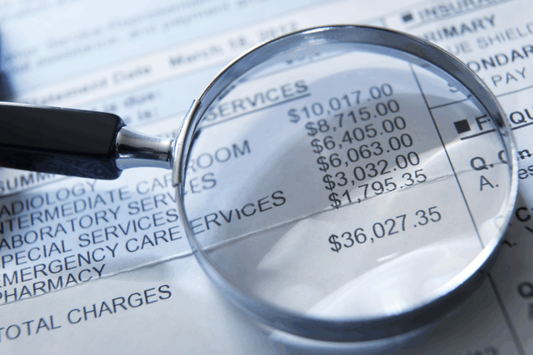 A magnifying glass rests on top of a medical invoice. Photographed with a very shallow depth of field.