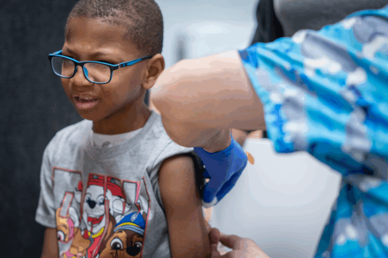 Xerius Jackson, age 7, gets an MMR vaccine at a clinic in Lubbock, Texas, on March 1. One sleeve of his T-shirt is rolled up as a health care worker vaccinates him.