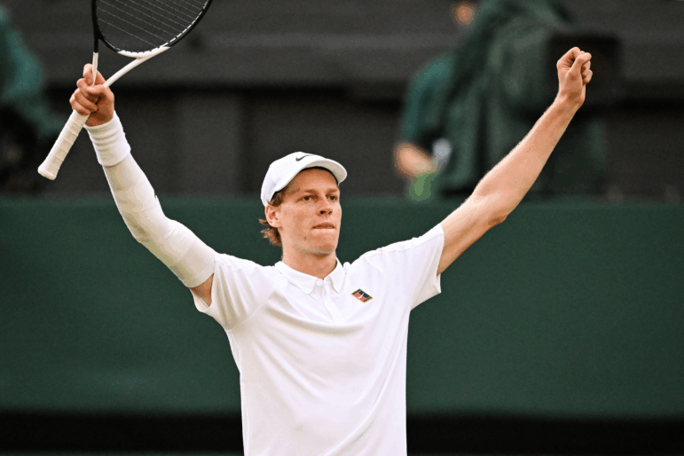 Italy's Jannik Sinner raises his arms and racket in celebration of his victory against Spain's Carlos Alcaraz at Wimbledon, southwest London, on Sunday. Sinner is wearing a white shirt and hat.