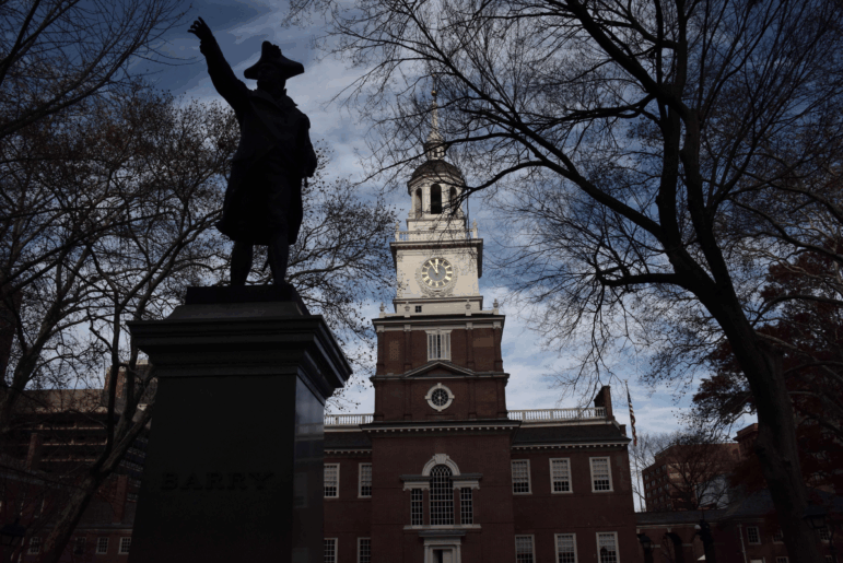 This photo shows Independence Hall in Philadelphia. The brick structure has a bell tower and steeple in the middle.
