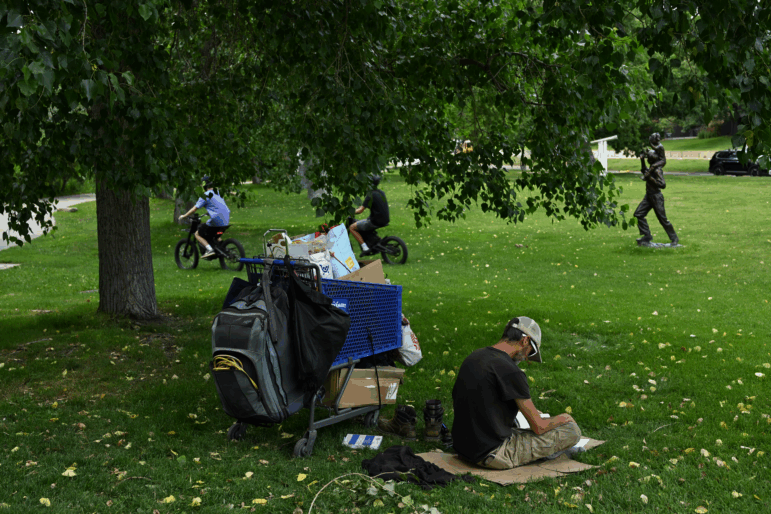 A man who identifies as homeless reads a book under the shade of a tree during high 90-degree temperatures last month in Boulder, Colo.