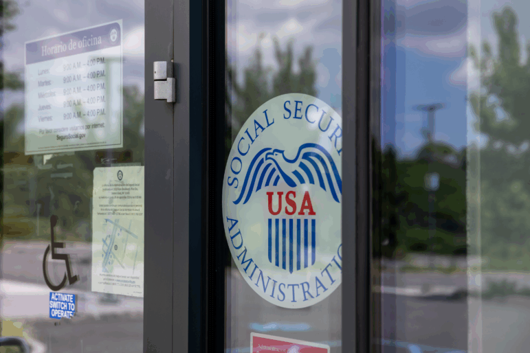 The entrance at a field office on Staten Island, N.Y., has a sign on the glass listing the hours and the Social Security Administration seal with an eagle and "USA" on it.