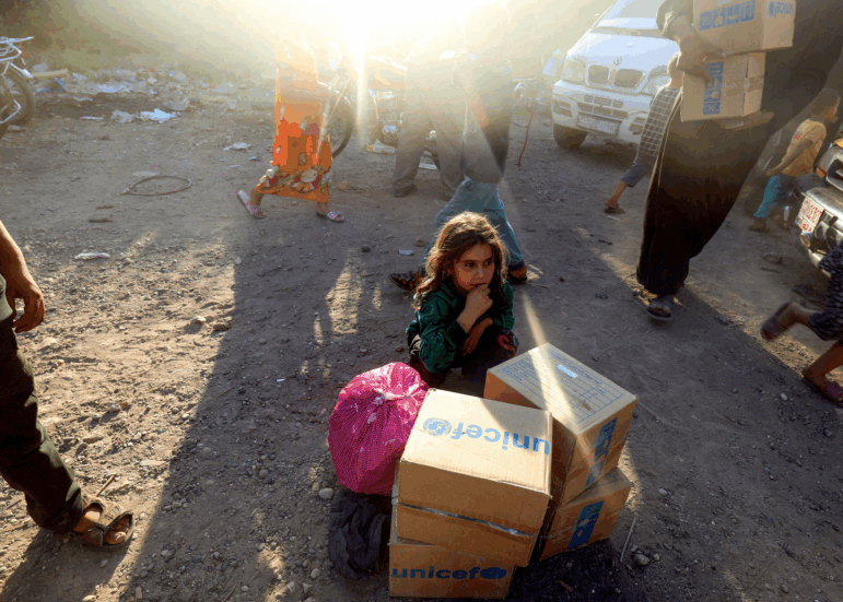 A picture taken on August 4, 2017 shows a displaced Syrian child, who fled from the Islamic State (IS) group's Syrian stronghold of Raqa, sitting behind humanitarian aid boxes delivered by UNICEF