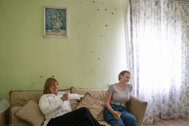 Iryna Schestova, 50, and her daughter, Liia Kazakova, 26, sit on a sofa in the living room of a friend's home in Horenychi, Ukraine.
