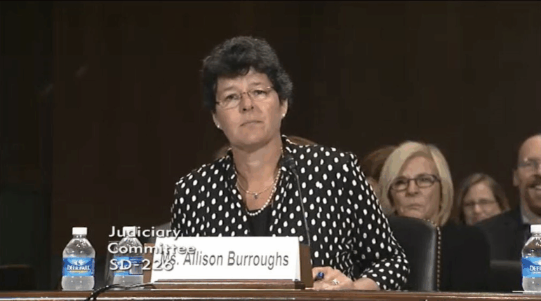 In this screenshot, Allison Burroughs is sitting at a table equipped with a microphone at her 2014 Senate confirmation hearing to be a U.S. district judge.