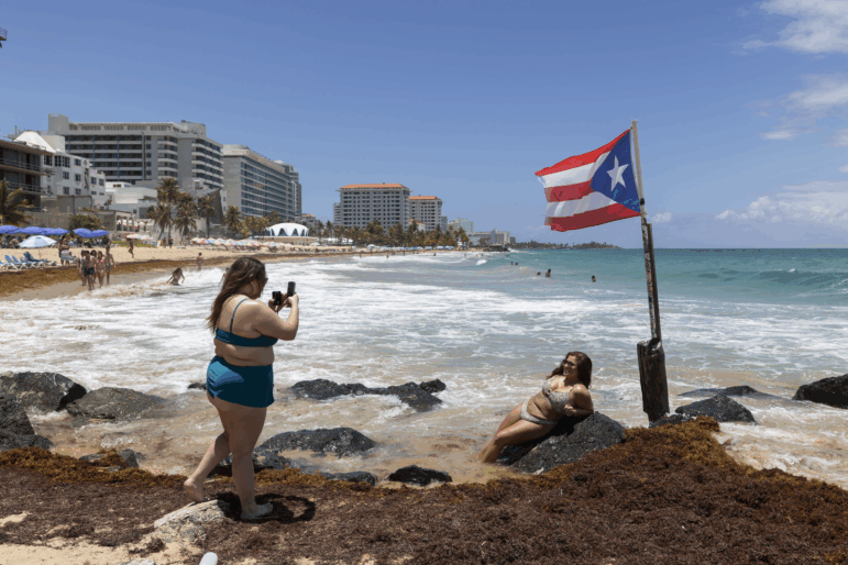 A woman poses for photos next to a Puerto Rican flag along the beach in Condado, Puerto Rico, as Hurricane Erin approaches, Friday, Aug. 15, 2025.