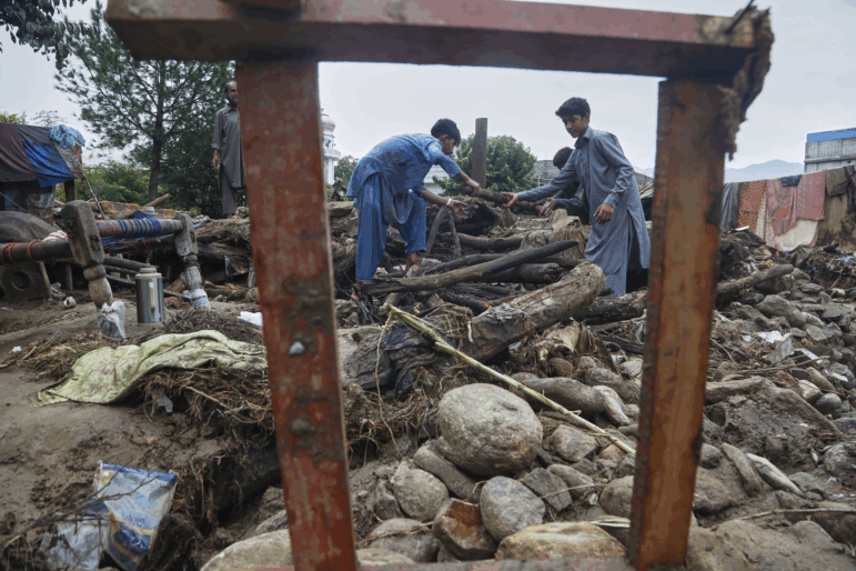 Boys collect wood and other useful items through the rubble of their damaged home following Friday's flash flooding at a neighborhood of Pir Baba, an area of Buner district, in Pakistan's northwest, on Aug. 17, 2025.
