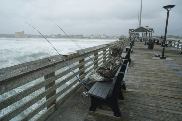 Sebastian Kettner fishes on Jennette's Pier as waves from Hurricane Erin crash ashore in Nags Head, N.C., on Thursday.