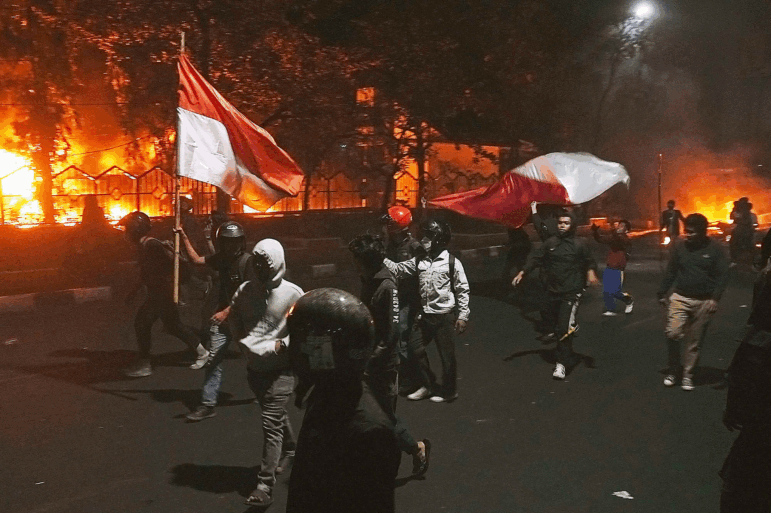 Protesters walk by as the local parliament building is engulfed in flames during a protest following the death of a delivery rider in clashes between riot police and students protesting against lawmakers' allowances in Makassar, South Sulawesi, Indonesia, Friday, Aug. 29, 2025.