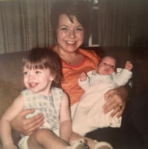 In this family photo, Ashley Ludlow's mother, Judy, is seated while holding Ludlow, who was a baby at the time, in her lap. Ludlow's sister, Whitney Peattie, who was a young girl at the time, is seated on the left side of the frame, and their mother has her arm around Peattie.