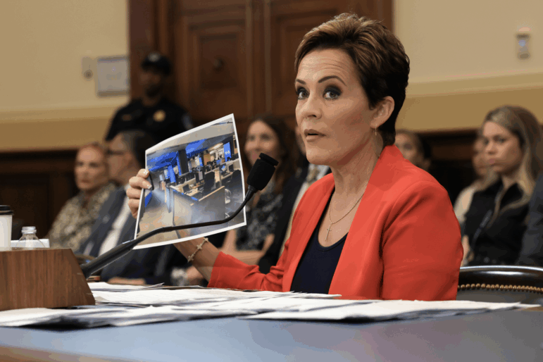 Trump adviser Kari Lake holds up a photograph, which she says shows an empty Voice of America (VOA) newsroom, as she speaks during a U.S. House Committee on Foreign Affairs hearing on June 25, 2025.