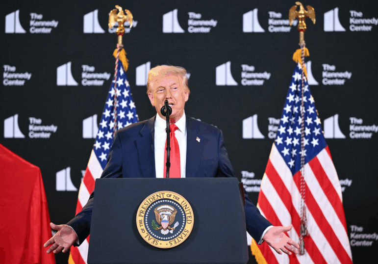 President Trump speaks from behind a lectern with the presidential seal on the front of it. Behind him are two American flags and a backdrop that says: "The Kennedy Center."