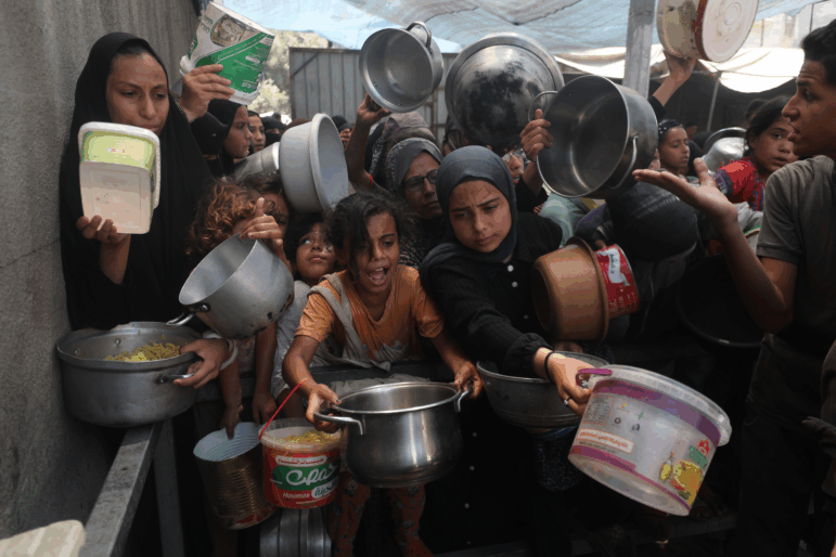 Palestinians, including children, who are struggling to access food due to Israel's blockade and ongoing attacks on the Gaza Strip, wait in line to receive food.