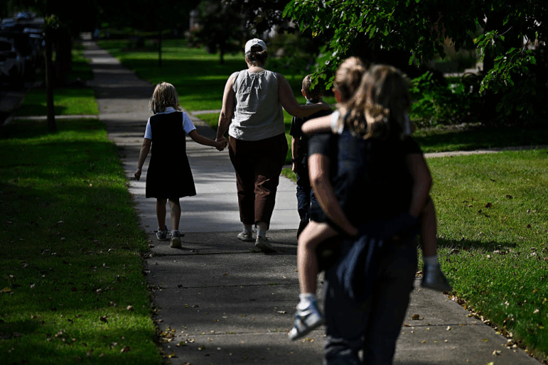 Families depart Annunciation Catholic School in Minneapolis following a mass shooting there on August 27, 2025. Parents are walking down a sidewalk with their children.