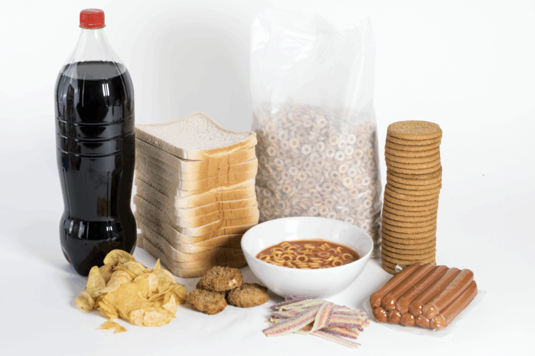 White bread, soda, crackers, cereal, canned spaghetti, hot dogs, chicken nuggets, chips and candy are pictured.