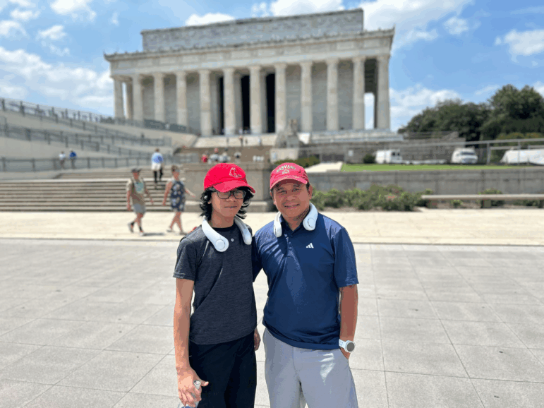Jeffrey Pagulong (right) and his 12-year-old son Christof stand near the Lincoln Memorial in Washington, D.C. They both wear red baseball caps and white neck cooling fans.