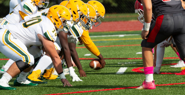 Side view of the center is snaping the ball at the start of a new play during a high school football game.