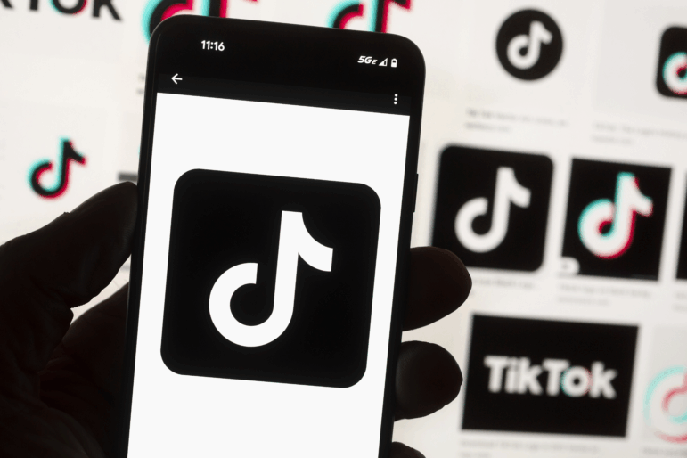 The TikTok logo is seen on a mobile phone in front of a computer screen which displays the TikTok home screen, Oct. 14, 2022, in Boston.